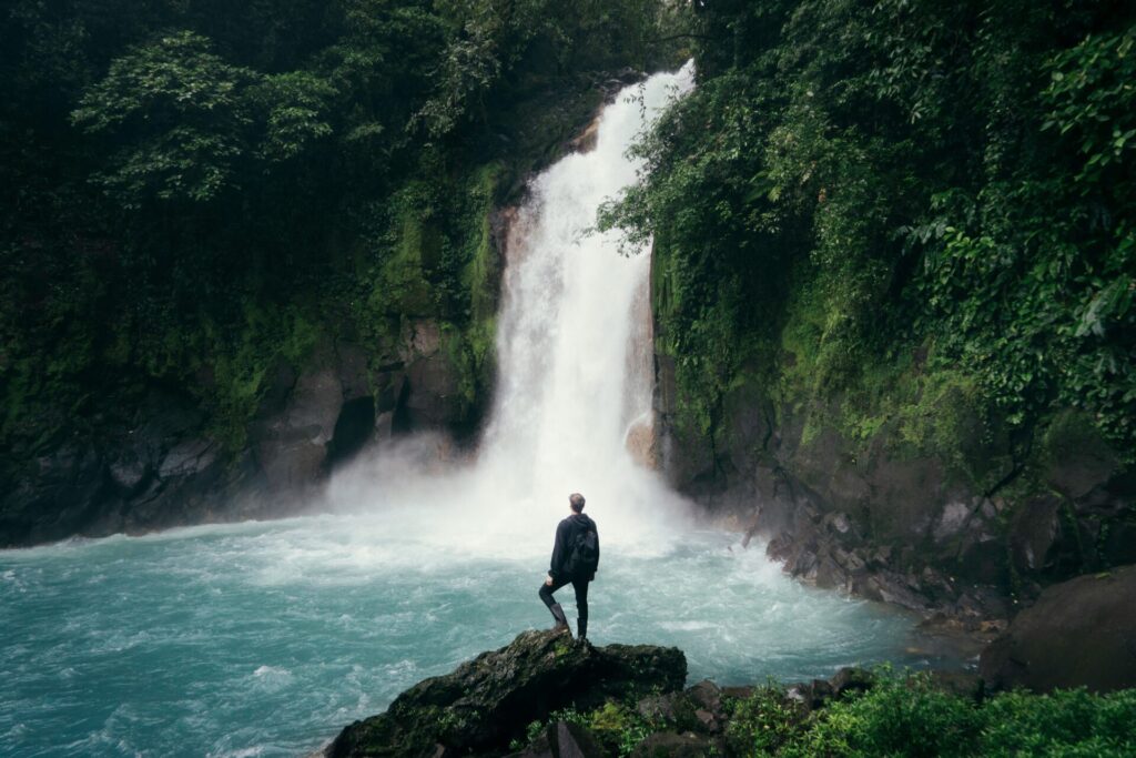 is-travel-insurance-worth-it Man standing in front of waterfall protected with travel insurance.